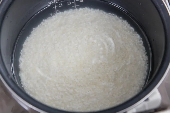 Để chuẩn bị nấu cơm cháy bằng nồi cơm điện tử, bạn vo sạch gạo rồi đổ nước và gạo theo tỷ lệ 1,5:1 hoặc 2:1 vào nồi cơm điện